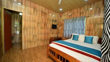 A bedroom with a wooden floor, a bed with a striped bedspread, a ceiling fan, and a television on a wooden stand.