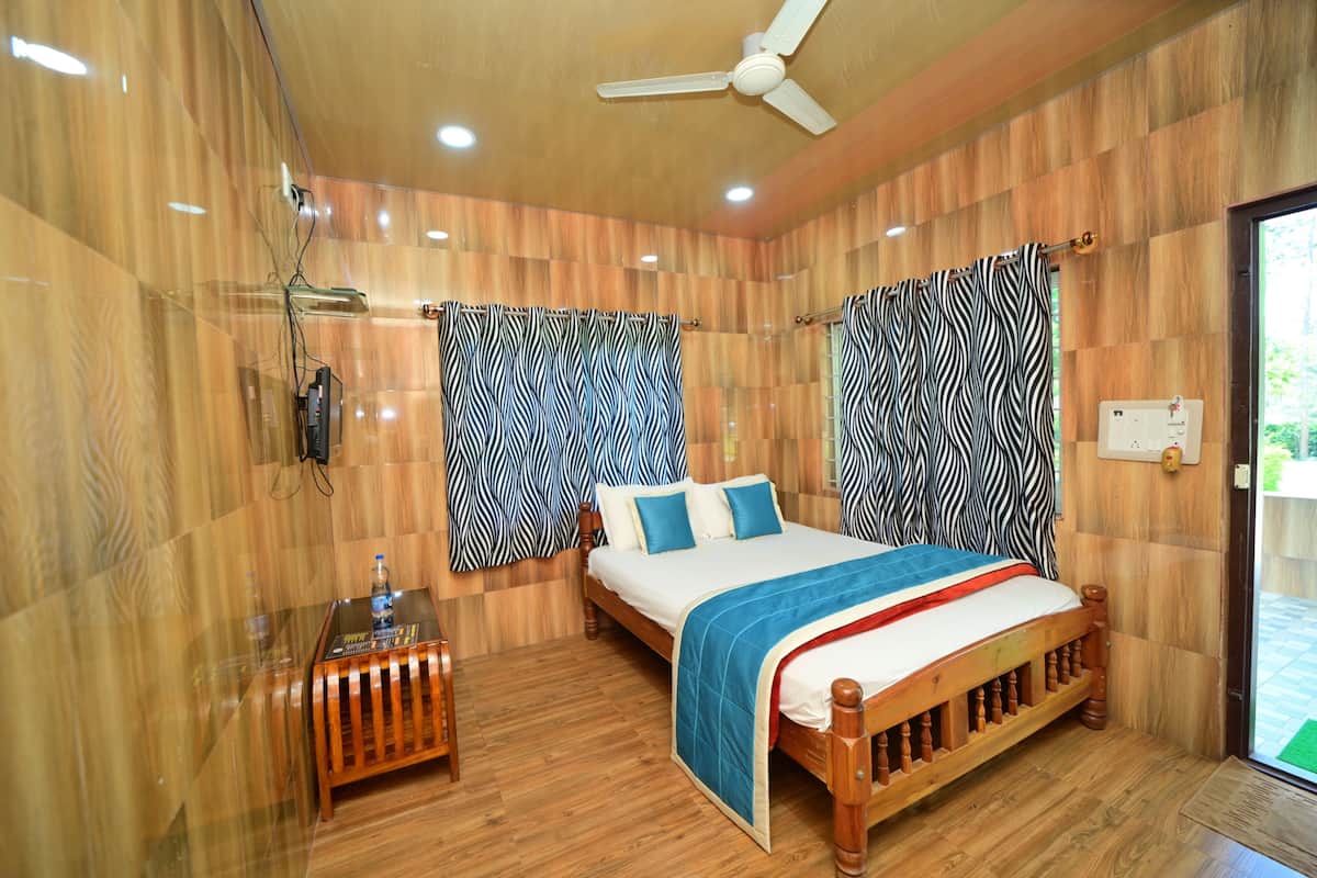 A bedroom with a wooden bed, zebra-patterned curtains, a ceiling fan, and a small table with a bottle.