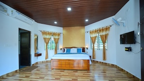 A bedroom with a wooden bed, a ceiling fan, an air conditioning unit, and a television on the wall.