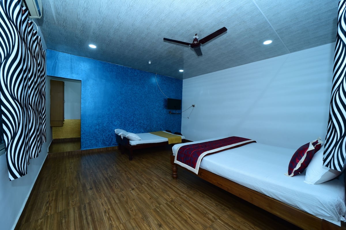 A room with two beds, a ceiling fan, and a blue accent wall.