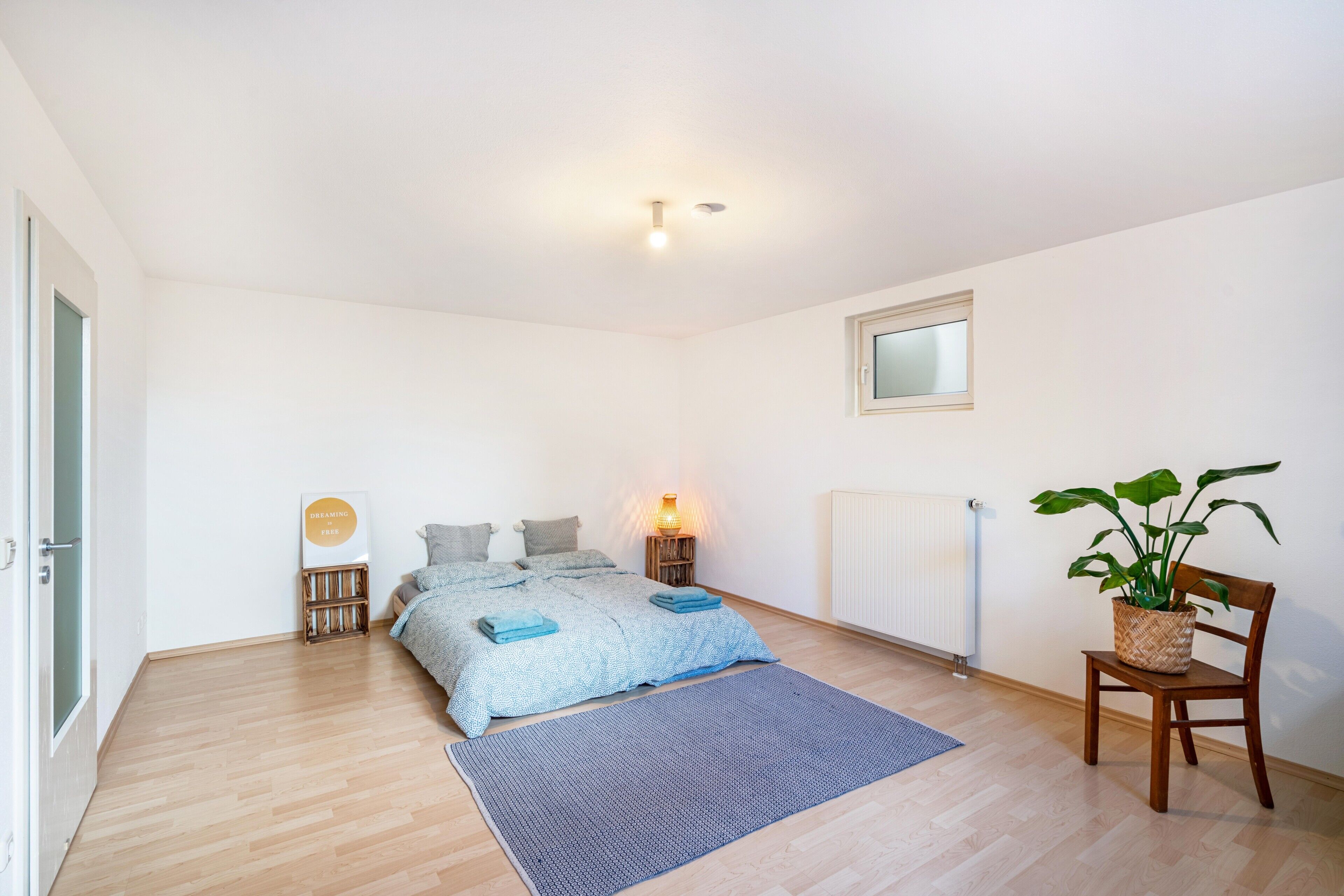 Un dormitorio con cama, mesita de noche, lámpara, radiador y una planta en maceta.