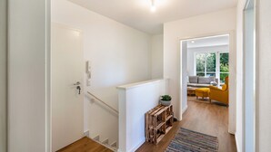 Un pasillo con suelo de madera, una puerta blanca y una escalera que lleva a una sala de estar con un sofá y un sillón amarillo.