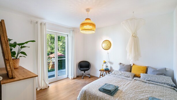 Un dormitorio con cama, una silla, un escritorio, una lámpara y una ventana con cortinas.