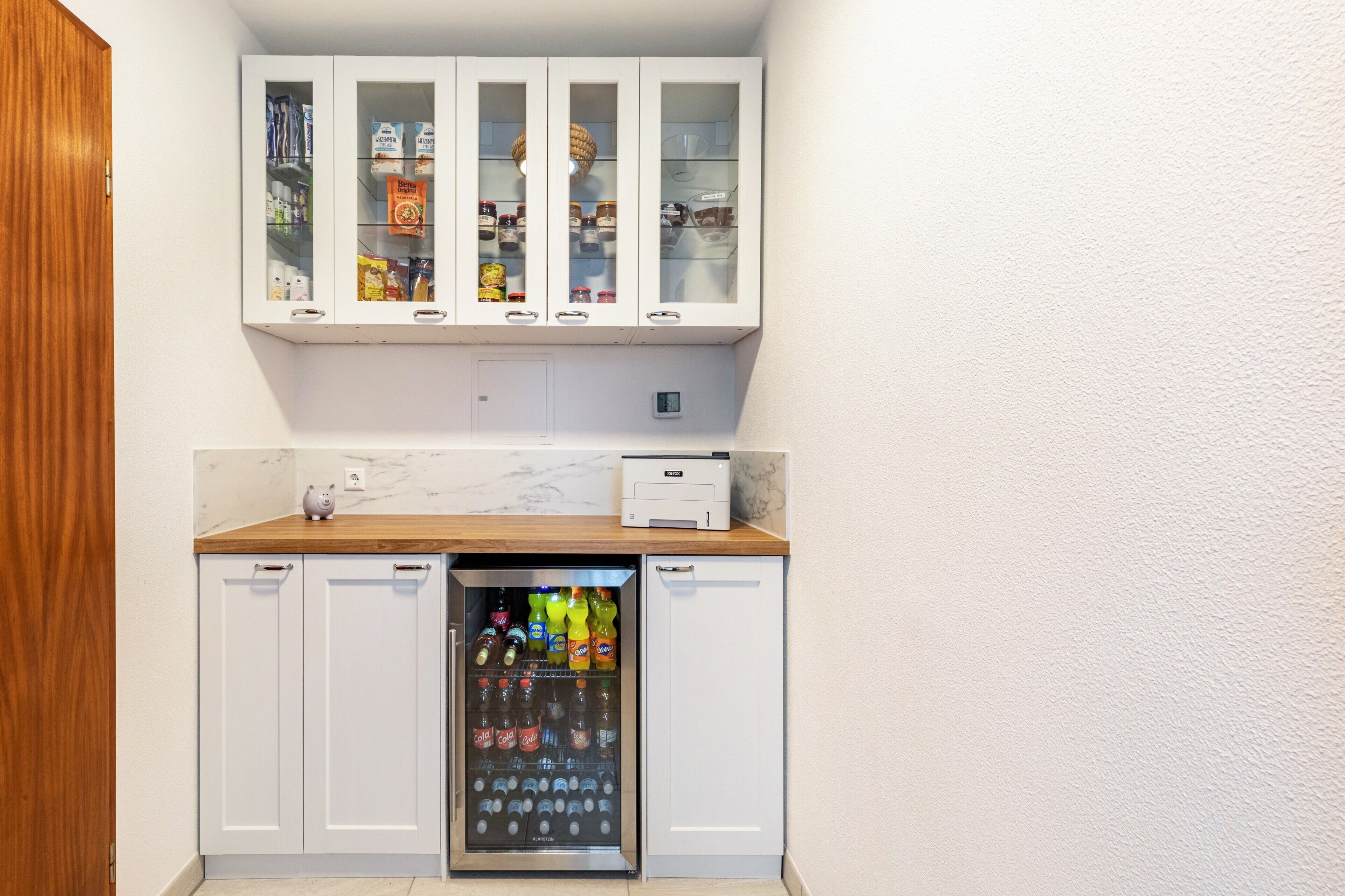 Cocina compacta con refrigerador, microondas y un mueble con puertas de vidrio.