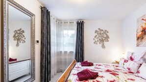 Ein Schlafzimmer mit einem Bett, einem Spiegel, Vorhängen und Wandbildern.