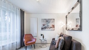 Ein stilvolles Wohnzimmer mit einer Couch, einem Sessel, einem kleinen Tisch und einem großen Spiegel.