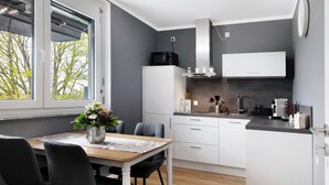 A modern kitchen with white cabinets, a dining table with chairs, a microwave, and a window with a view of trees. - Holiday Apartment "B5" with Mountain View, Balcony & Wi-Fi (Bad Bellingen)