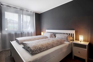 A double bed with a headboard, bedside lamps, and a window with blinds. - Holiday Apartment "B5" with Mountain View, Balcony & Wi-Fi (Bad Bellingen)