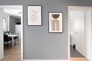 A hallway with a framed abstract art piece on the wall, a dining area with a table and chairs, and a white door leading to another room. - Holiday Apartment "B5" with Mountain View, Balcony & Wi-Fi (Bad Bellingen)