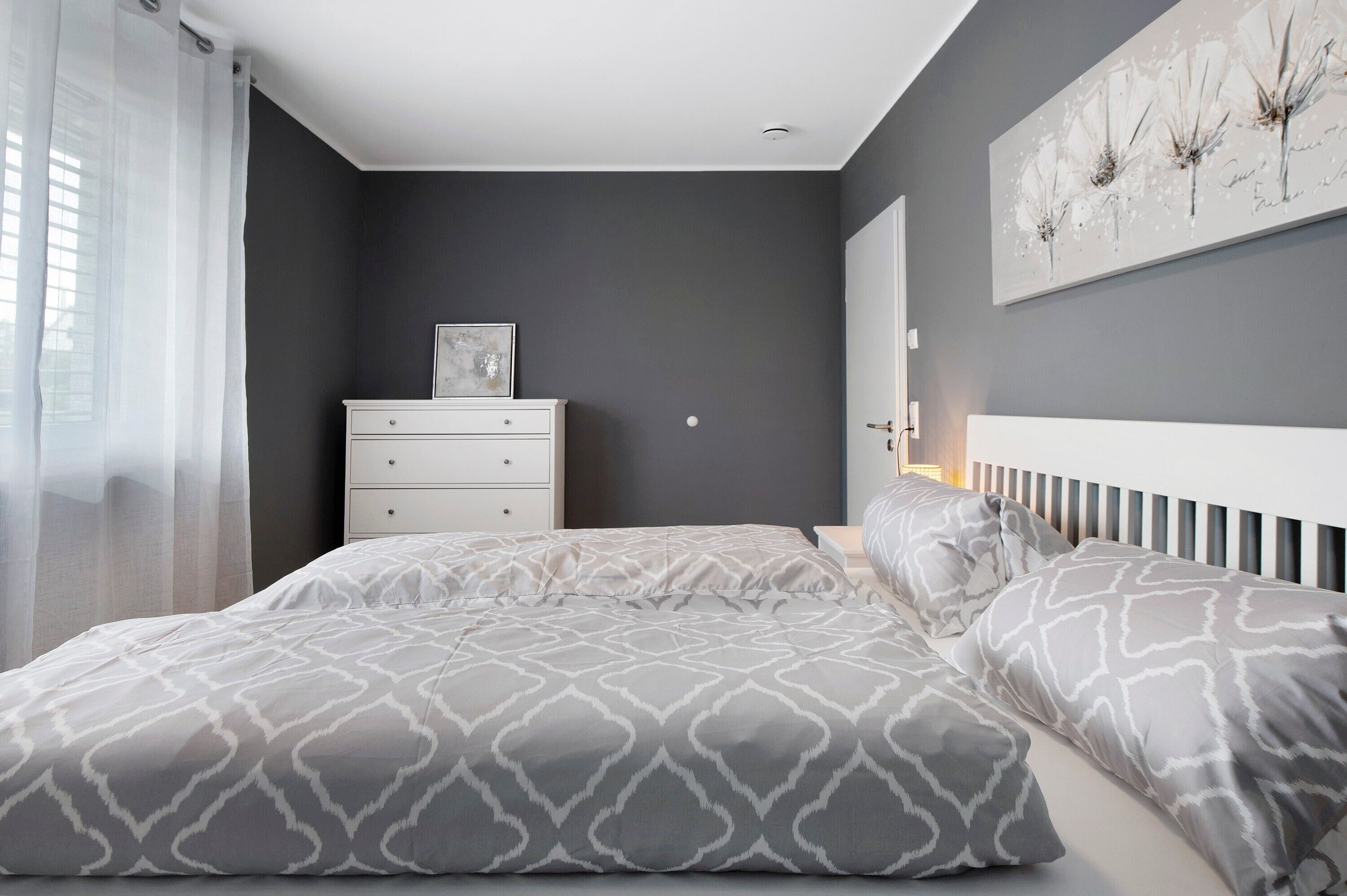 Un dormitorio con cama, cómoda, radiador y un cuadro floral en la pared.