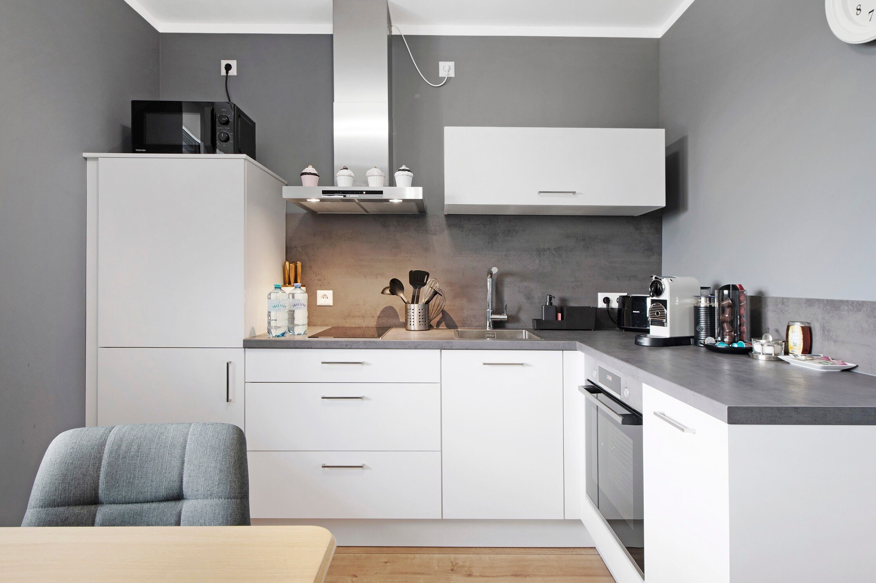A modern kitchen with white cabinets, a microwave, a coffee machine, and a sink.