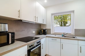 Una cocina moderna con armarios blancos, horno empotrado, estufa y ventana con vista a árboles.