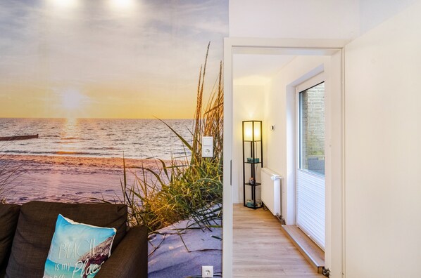 A beach-themed wall mural, a modern interior with a floor lamp, and a view through a window.