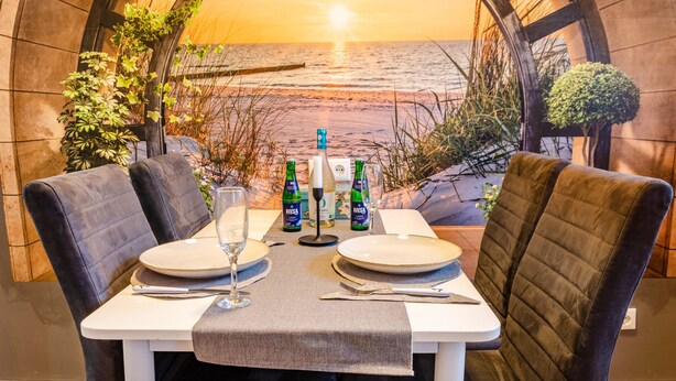 A dining table set with plates, cutlery, and drinks, with a view of the ocean through an arched window.