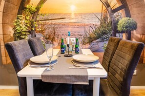 A dining table set with plates, cutlery, and drinks, with a view of the ocean through an arched window.