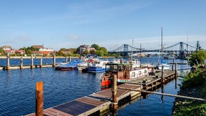 A marina with boats docked, a bridge in the background, and houses along the water.