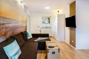 Una sala de estar moderna con un sofá, una mesa de centro, un televisor y una ventana con vistas a árboles.