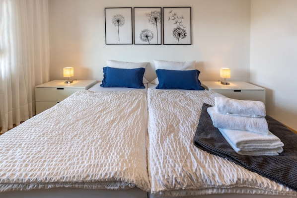A double bed with white bedding, two blue pillows, a bedside table with a lamp, and three framed pictures on the wall. - Apartment 'Fewo Stempel' with Private Terrace, Private Garden and Wi-Fi (Küssaberg)