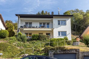 A two-story residential building with a balcony, a garage, and a hillside setting. - Apartment 'Fewo Stempel' with Private Terrace, Private Garden and Wi-Fi (Küssaberg)