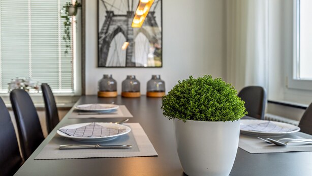 Una mesa de comedor con platos, cubiertos y una planta en maceta.