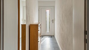 Un pasillo con un armario de madera, una puerta con ventanal y un suelo de tonos claros.