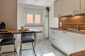 A modern kitchen with a wooden countertop, two black chairs, a built-in sink, and a window with blinds. - Apartment 'Fewo Stempel' with Private Terrace, Private Garden and Wi-Fi (Küssaberg)
