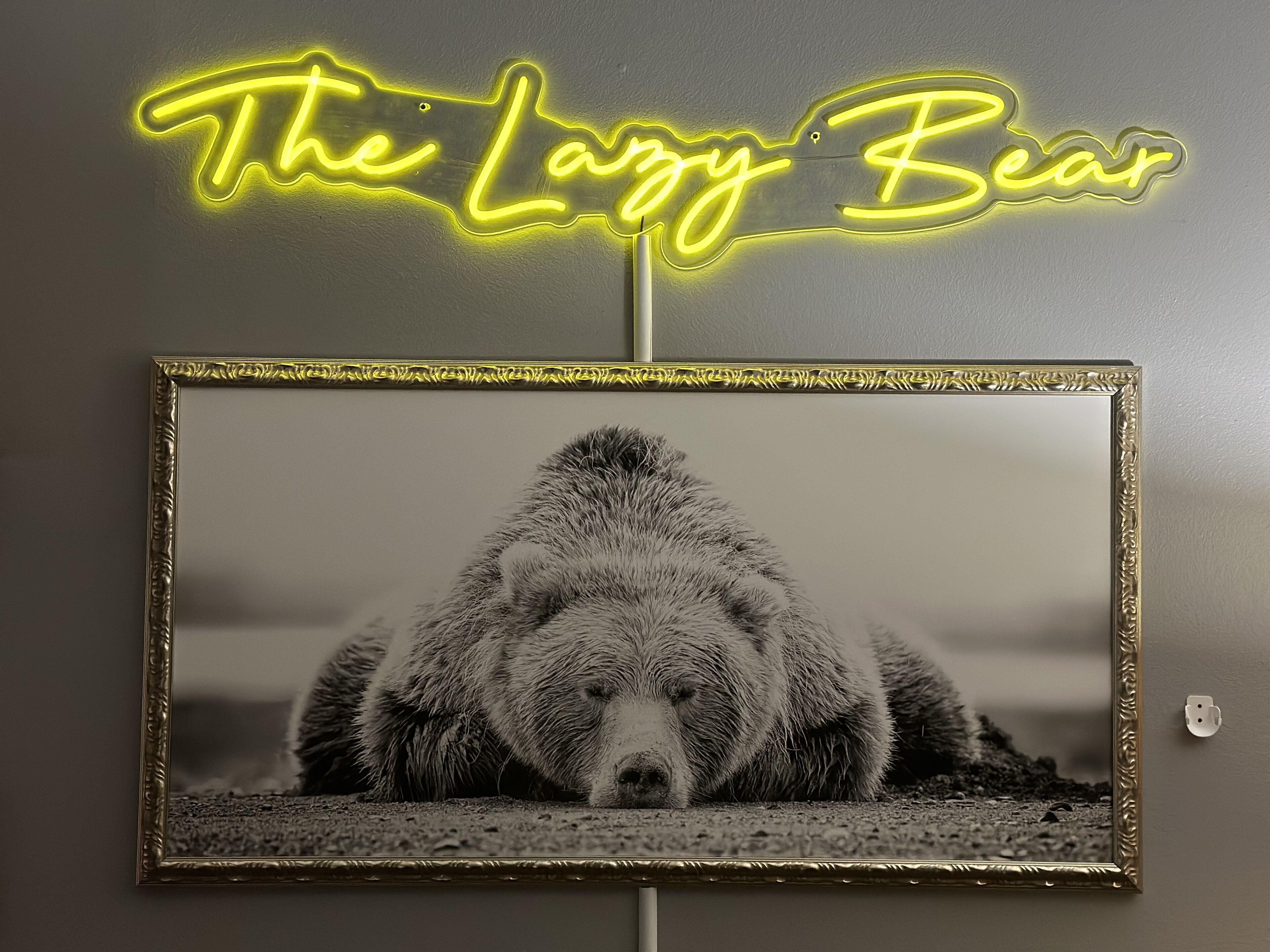 A framed photograph of a bear with a neon sign above it that reads "The Lazy Bear".