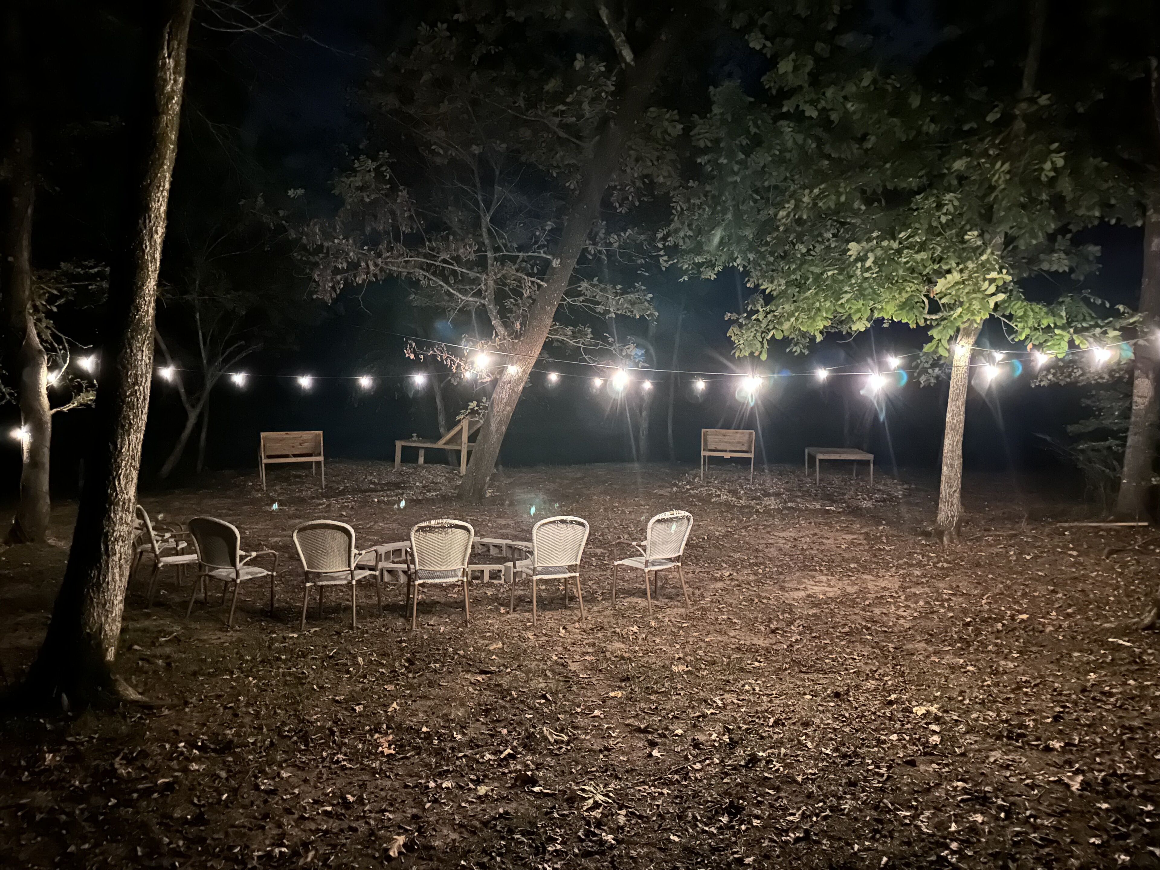 An outdoor seating area with string lights, surrounded by trees.