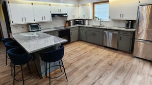 Een moderne keuken met witte kasten, een centraal eiland met barstoelen, een roestvrijstalen koelkast en een magnetron.