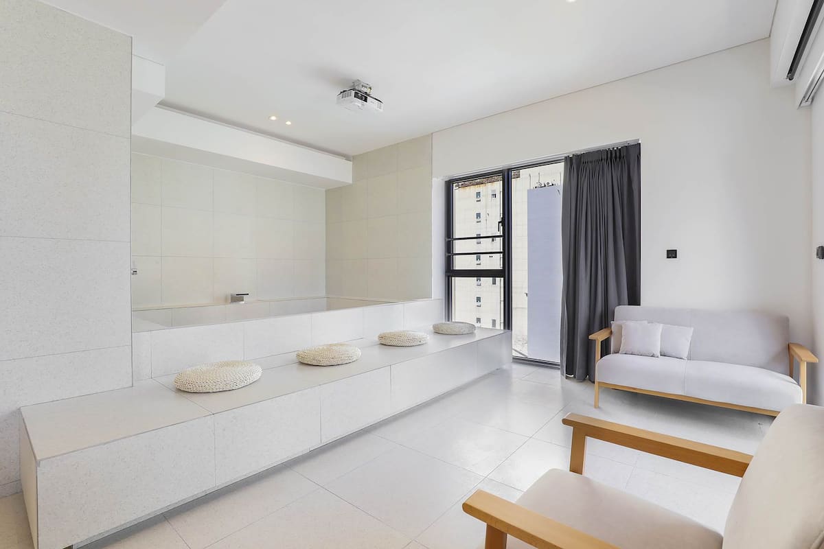 A modern living room with a white sofa, a wooden bench, and a large window with curtains.