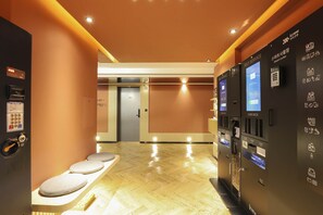 A hotel lobby with a reception desk, self-service lockers, and a seating area.