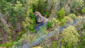 A house surrounded by dense forest with a visible driveway leading to the entrance. - Moonshine Mountain | Hot tub & fire pit | Bryce Resort (Basye)