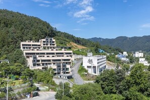 A modern building with multiple floors, surrounded by lush greenery and hills. - Caserio Resort (Gapyeong)