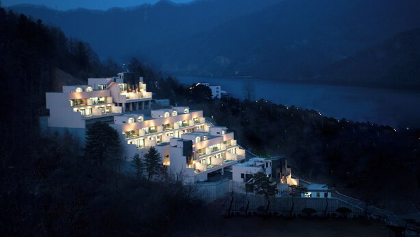 Un hôtel à plusieurs étages, doté de nombreux balcons et offrant une vue sur un lac au crépuscule.