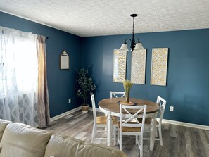 Un coin repas avec une table ronde, des chaises blanches, un vase agrémenté de verdure et des œuvres d’art murales à motifs.