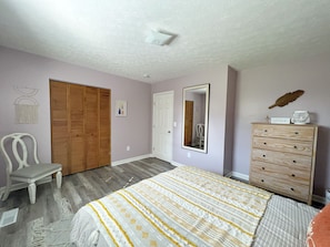 Une chambre à coucher avec un lit, une armoire en bois, une chaise, une commode et un miroir au mur.