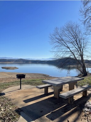 Un espace pique-nique équipé de bancs et d’une boîte aux lettres, offrant une vue sur un lac paisible avec des montagnes en arrière-plan.