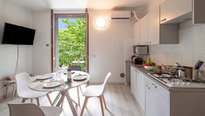 A modern kitchen with white cabinets, a gas stove, and a dining area with white chairs and a table set for two. - Porto Letizia Mozart 6, Porlezza, Italy (Porlezza)