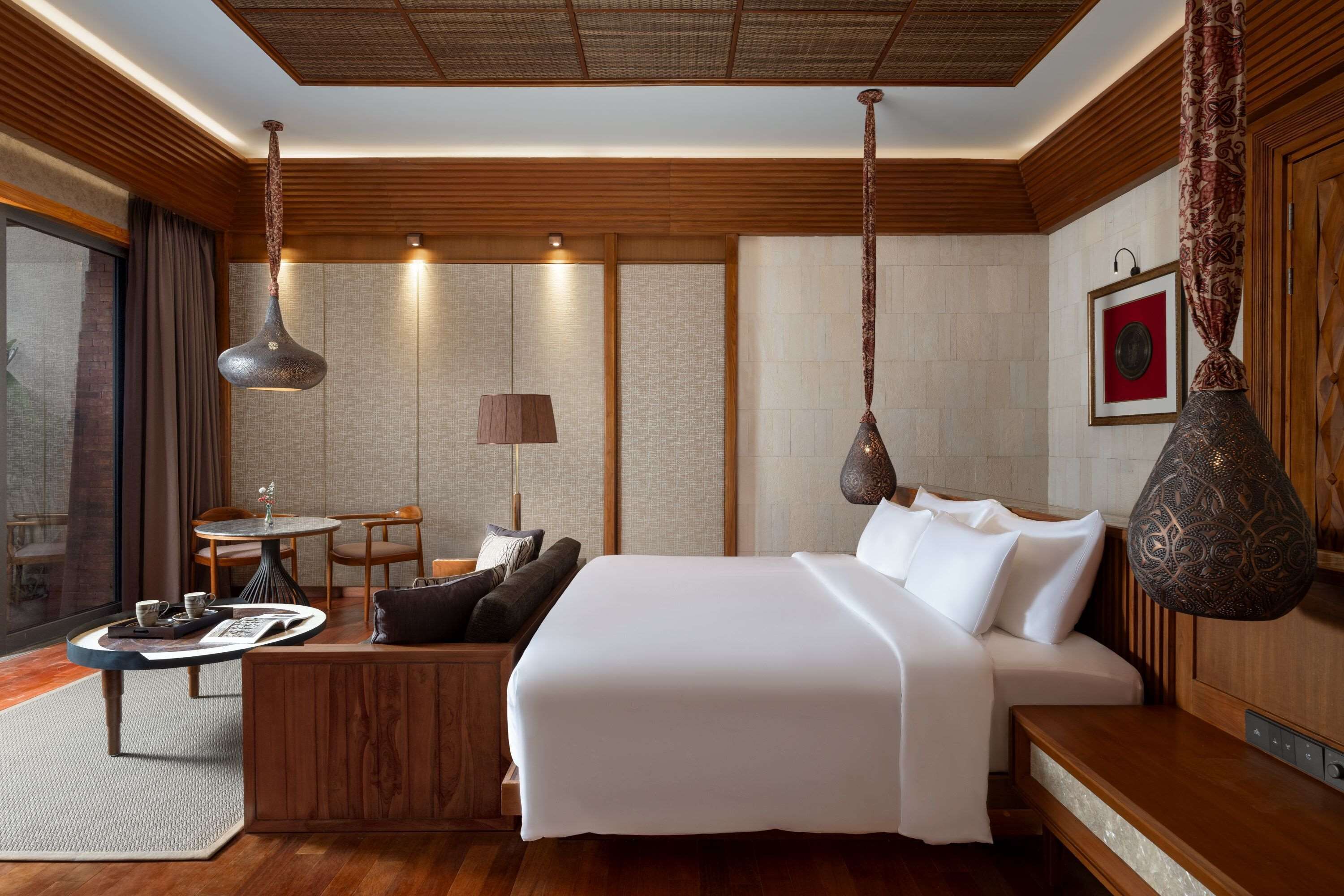 Quarto de hotel com uma cama grande, uma mesa de jantar, um sofá e um candeeiro suspenso.