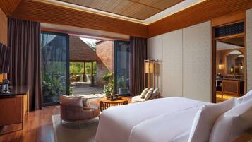 Habitación de hotel con una cama grande, un escritorio, una silla y vistas a un jardín por la puerta corrediza de vidrio.