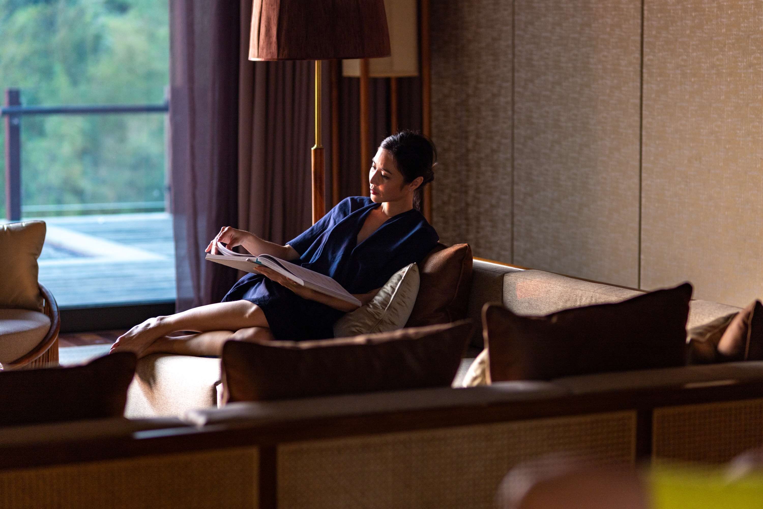 A person sitting on a sofa in a room with a view of greenery outside.