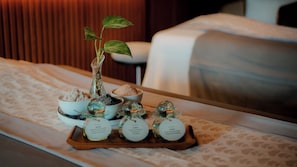 A tray with various items including a potted plant, bowls of salts, and glass containers on a bed.