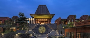 A modern building with a central atrium, stone steps leading up to it, and a pool area in front.
