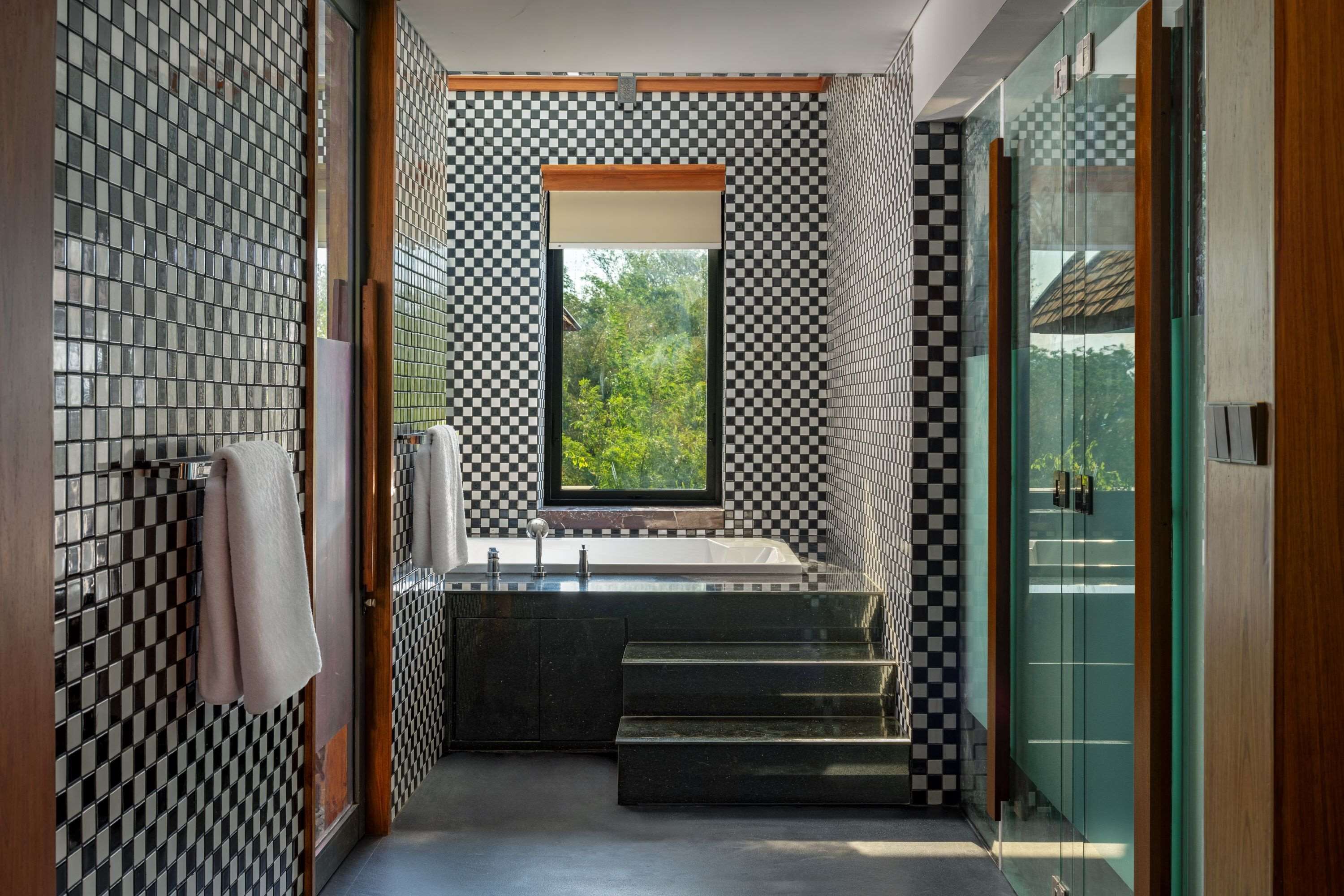 Un bagno moderno con una parete rivestita di piastrelle a scacchi, un'ampia finestra e un box doccia in vetro.
