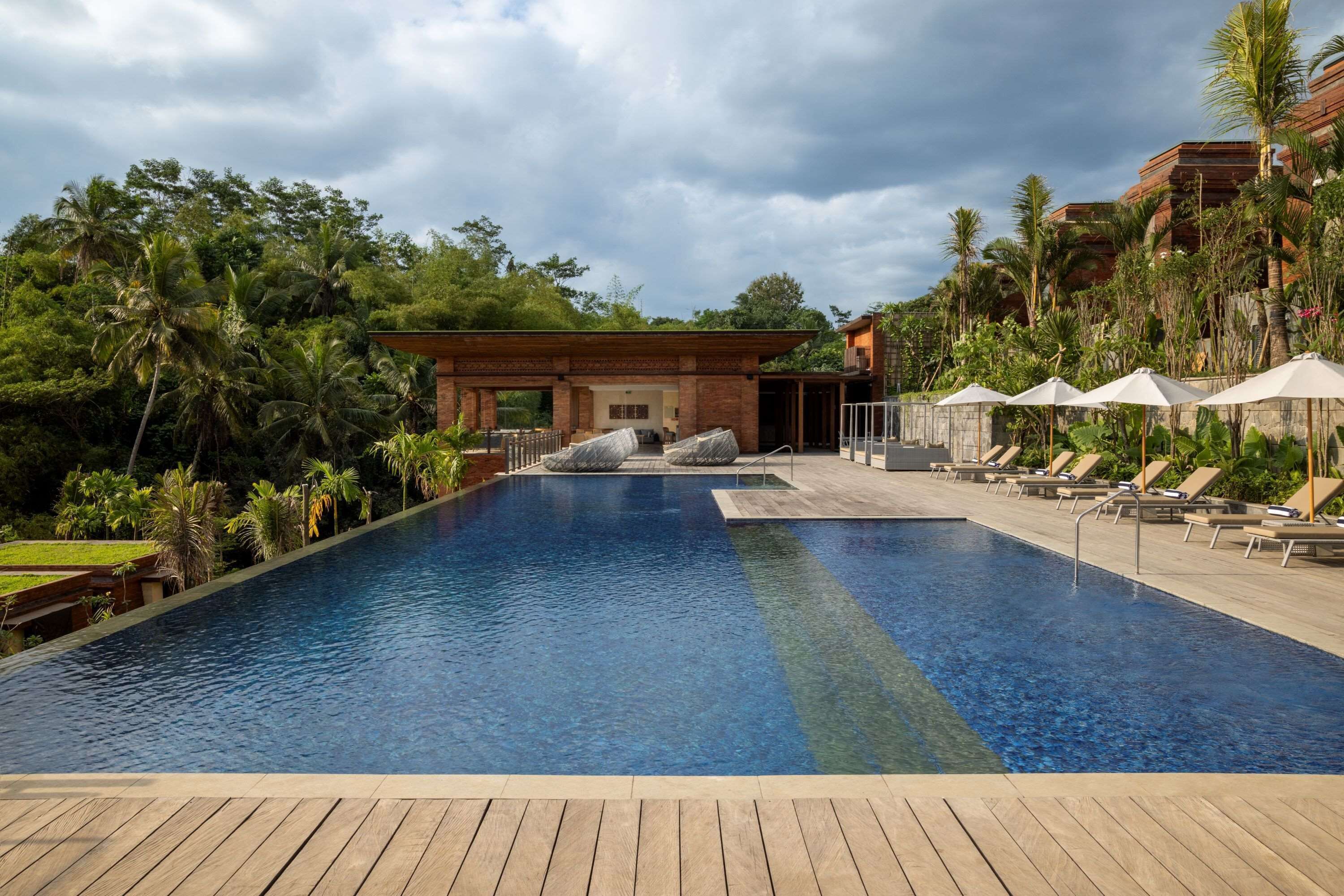 Piscina com deck de madeira em primeiro plano, rodeada por espreguiçadeiras e guarda-sóis.