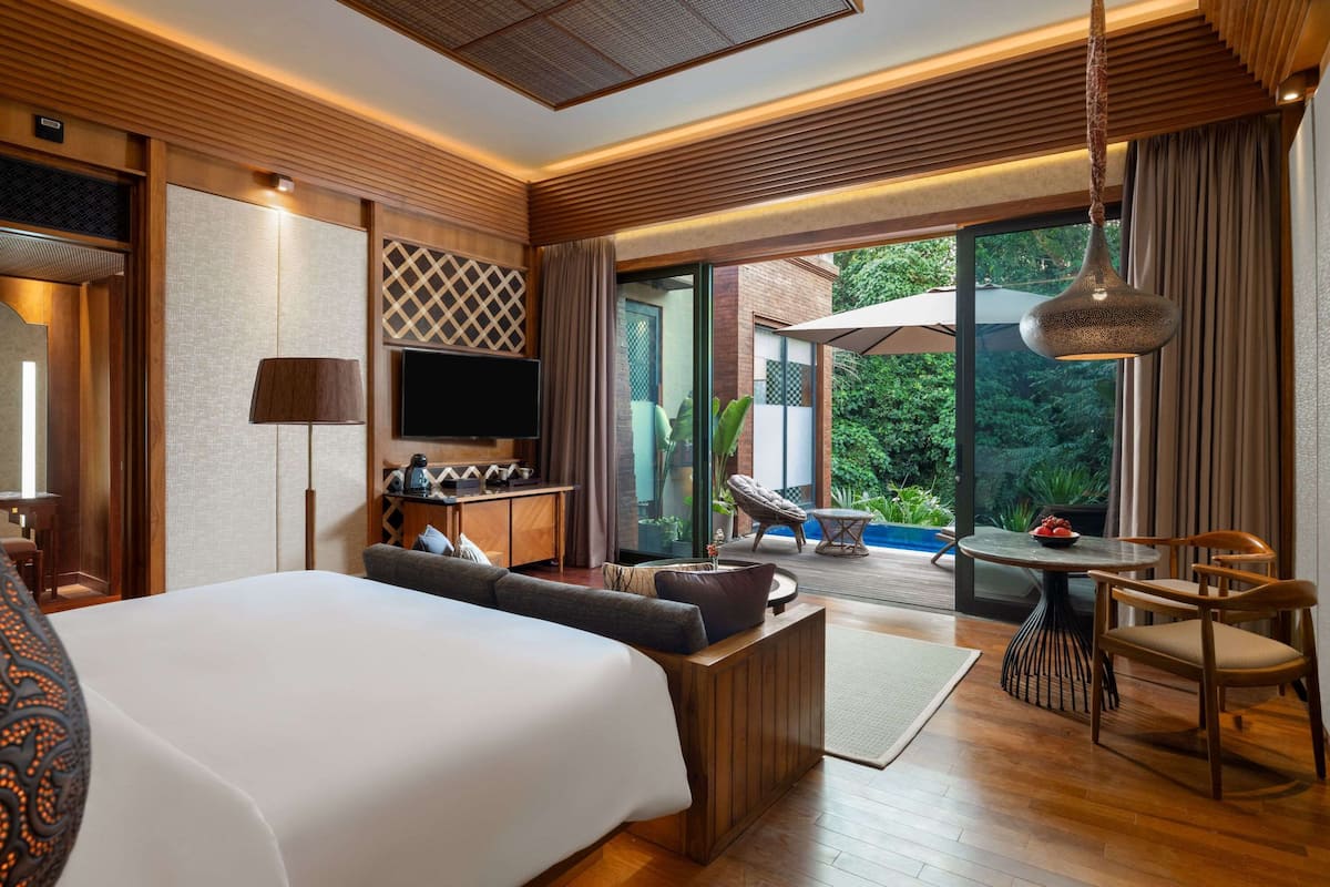 A modern hotel room with a large bed, a TV, a seating area with a table and chairs, and a view of the outdoors.