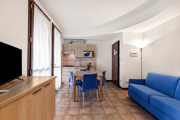 A compact living space with a TV, dining table, chairs, a sofa, a kitchen area, and a sliding door. - Porto Letizia Torino 5, Porlezza, Italy (Porlezza)