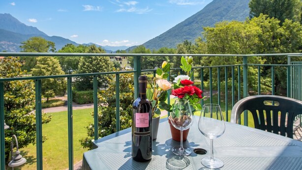 A balcony with a table, a bottle of wine, a glass, and a vase with flowers.