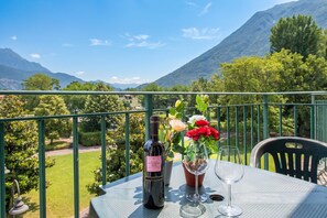 Un balcon avec une table, une bouteille de vin, un verre et un vase rempli de fleurs.