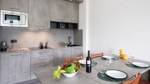 A modern kitchen with grey cabinets, a built-in microwave, and a dining area set with white plates, glasses, and a bottle of wine.